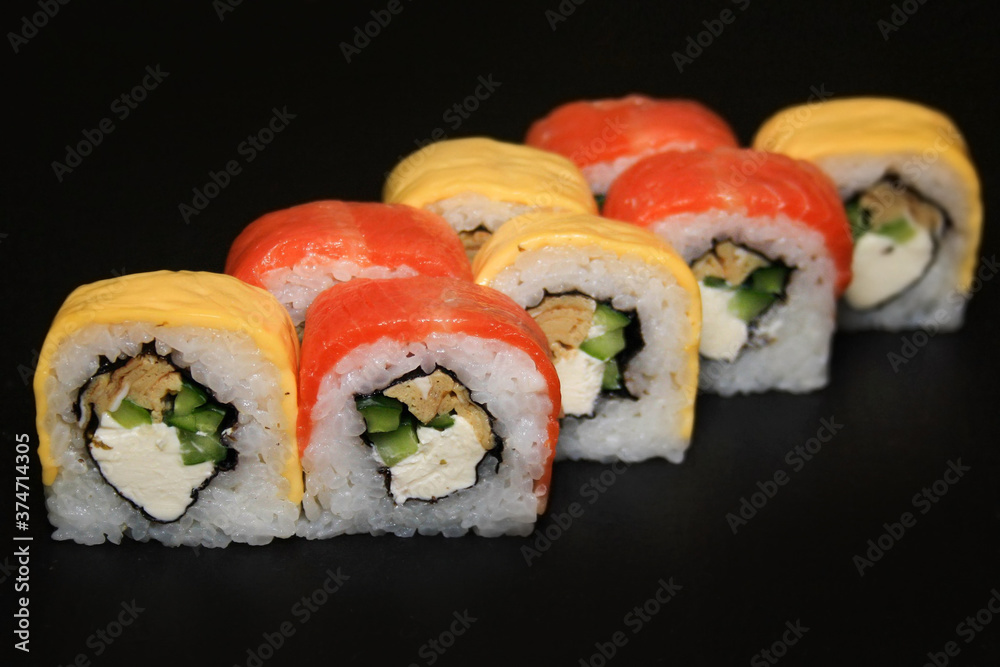 Multicolored sushi roll with salmon, cheese, cucumber and omelet on black background. Multicolored sushi roll with salmon, cheese, cucumber and omelet on black background.