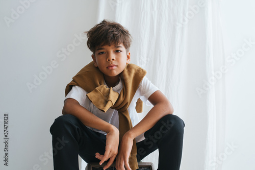 Φωτογραφία Emotionless indian asian kid looking at the camera, sitting low, knees up