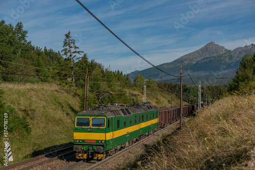 Green electric cargo train under Vysoke Tatry mountains in summer morning