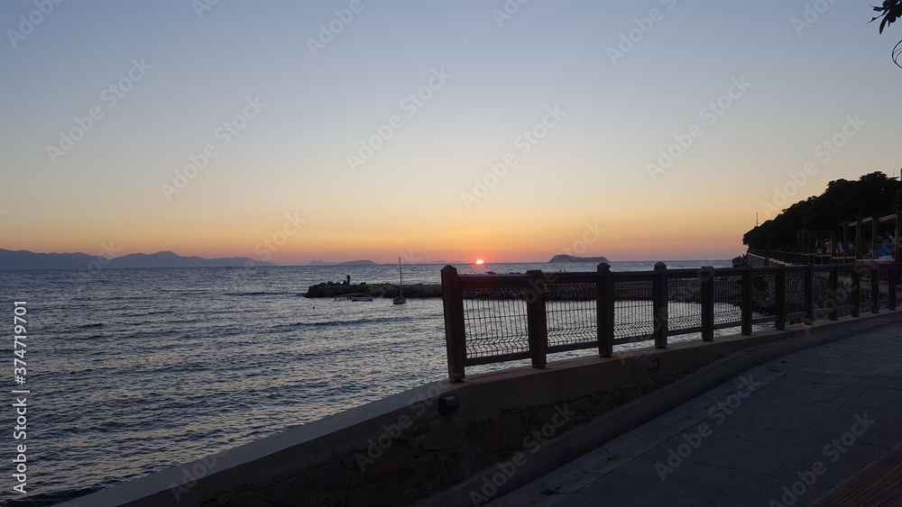 Sunset view from the Mediterranean coast. Sunset visible over the breakwater in the calm sea on the horizon. Mediterranean waves calmly hitting the shore. Mediterranean sea with beautiful sunset.