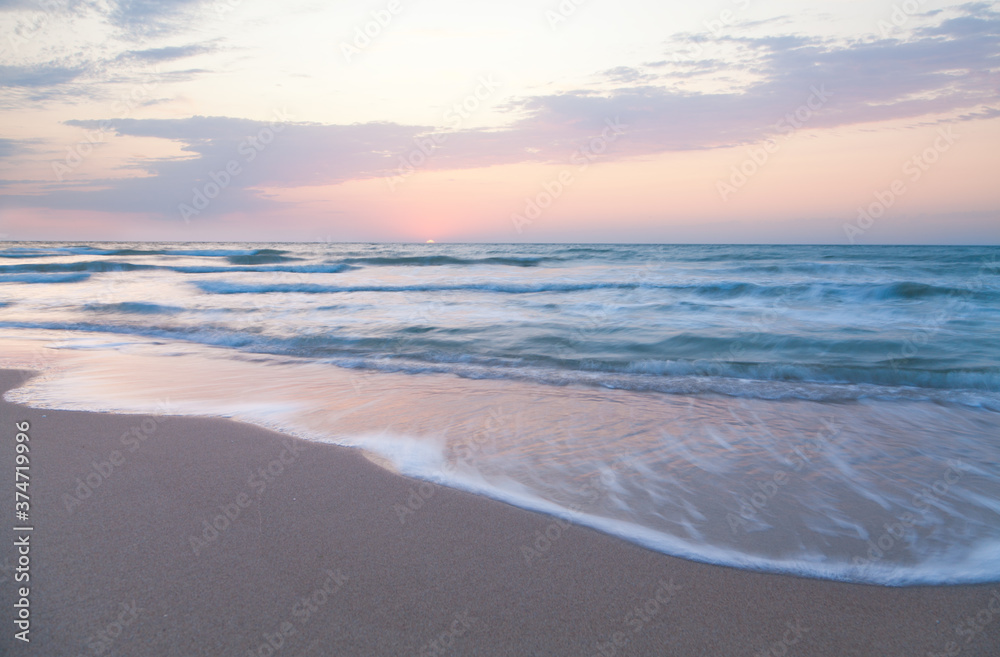 Waves washing the sandy sea beach at sunrise.