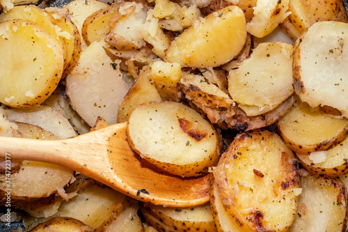 Hot baked potato slices with thin-skinned potatoes with a wooden spoon. A simple and quick after-work meal for the worker and bachelor