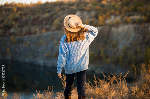 Autumn girl in blue sweater and hat standing backwards and admire nature lake view. Autumn forest colors with girl back view.