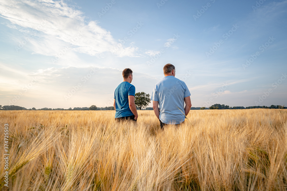 Landwirtschaft - Agrarpolitik, nachdenklicher Landwirt mit seinem Sohn im Getreidefeld Landwirtschaft - Agrarpolitik, nachdenklicher Landwirt mit seinem Sohn im Getreidefeld