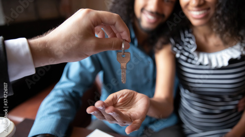 Close up happy young African American couple receiving keys from realtor  real estate agent  overjoyed family husband and wife purchasing first apartment  buying new house  making deal at meeting