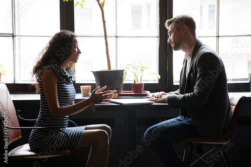 Smiling African American woman financial advisor consulting man client at meeting in cafe, sitting at table with laptop, female candidate answering employer executive questions on job interview