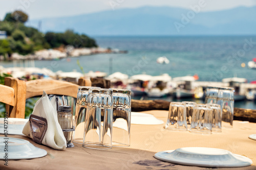 Φωτογραφία Glasses and plates on a wooden table of a greek tavern over the view of the port of Amaliapoli, Greece