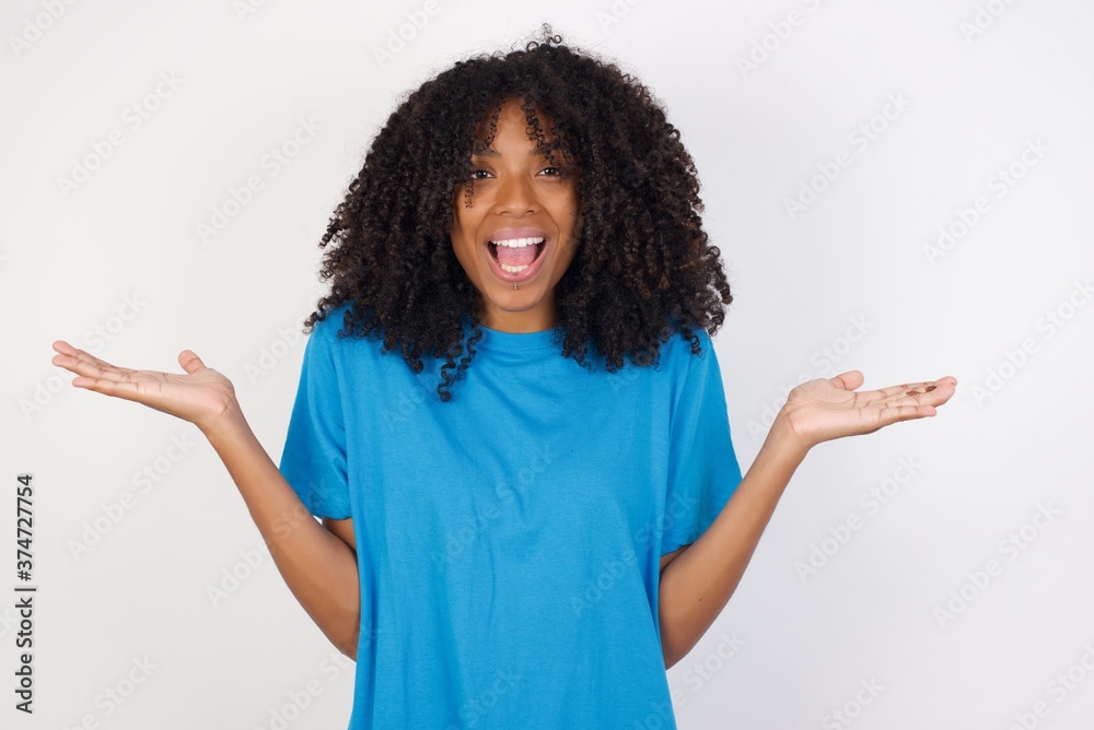 Young african woman with curly hair wearing casual blue shirt over white background celebrating crazy and amazed for success with arms raised and open eyes screaming excited. Winner concept Young african woman with curly hair wearing casual blue shirt over white background celebrating crazy and amazed for success with arms raised and open eyes screaming excited. Winner concept