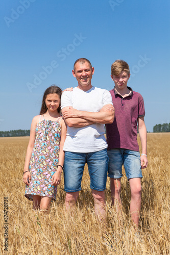 Dad with preteen son and daughter, full length portrait, Caucasian single father with two children standing on wheat field at summer