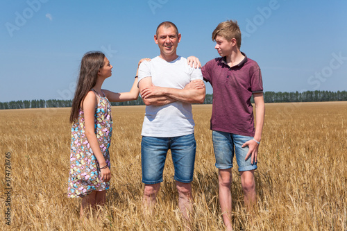 Preteen son and daughter looking at their single father, kids lay hands on his shoulders, wheat field