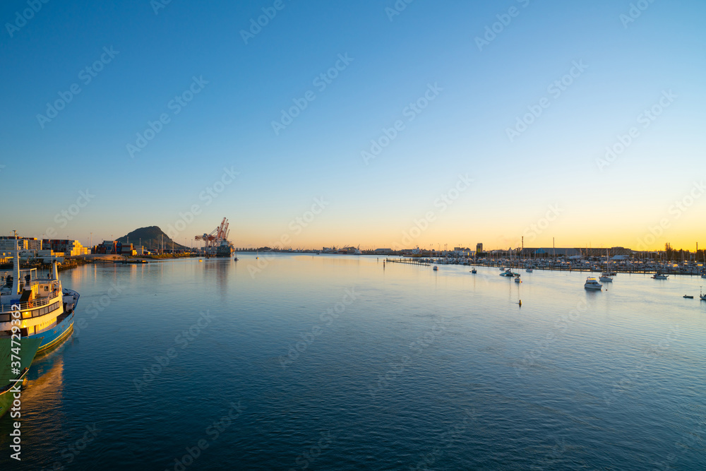 Tauranga harbour at sunrise with port facilities and landmark Mount Maunganui on golden horizon