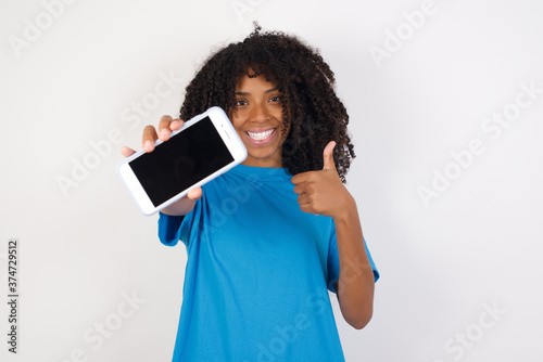 Portrait Young african woman with curly hair wearing casual blue shirt, holding in hands cell showing giving black screen thumb up