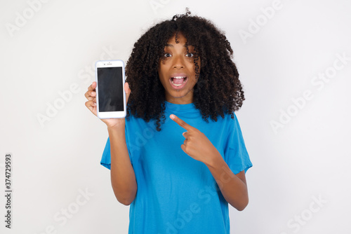 Attractive cheerful Young african woman with curly hair wearing casual blue shirt holding in hands cell showing black screen