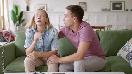 young married lover couple sit on couch at home talking. woman is upset and frustrated due to worries and problems. man consoles and supports. husband apologizes to offended wife