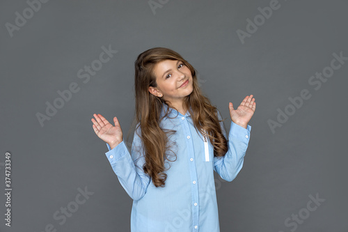 Beautiful cheerful schoolgirl girl in shirt points to empty space on gray background for text or message. Positive smile, emotions of joy and satisfaction. Concept education. Studio shot. Copy space