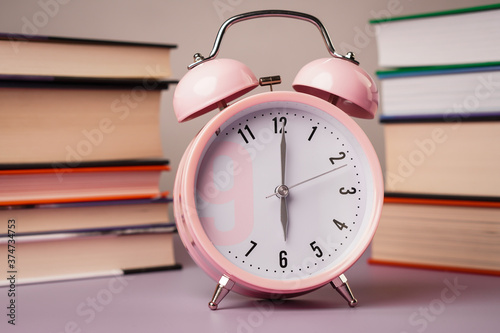 Time to school. Detail close up of the old pink vintage alarm. In the background are old books.