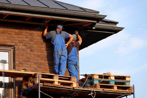 Workers during roofing  two builders on scaffolding standing near the building wall. Construction and repair works of a house