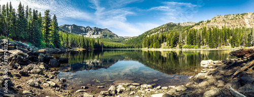 Photo Panorama of a mountain lake with rocks in the foreground and trees in the far shore with mountains in the background, blue sky with high clouds