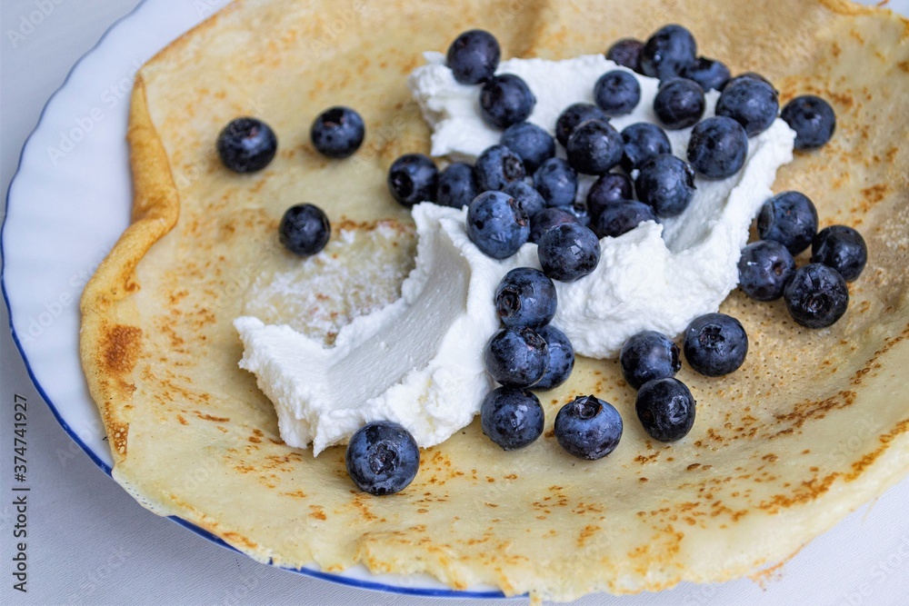 Composition in natural light. Black currant filling (focus is not on all berries) and soft cheese in a large homemade pancake Composition in natural light. Black currant filling (focus is not on all berries) and soft cheese in a large homemade pancake