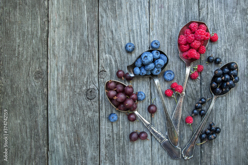 Gooseberries, black currants, raspberries and blueberries in spoons on a wooden old background.