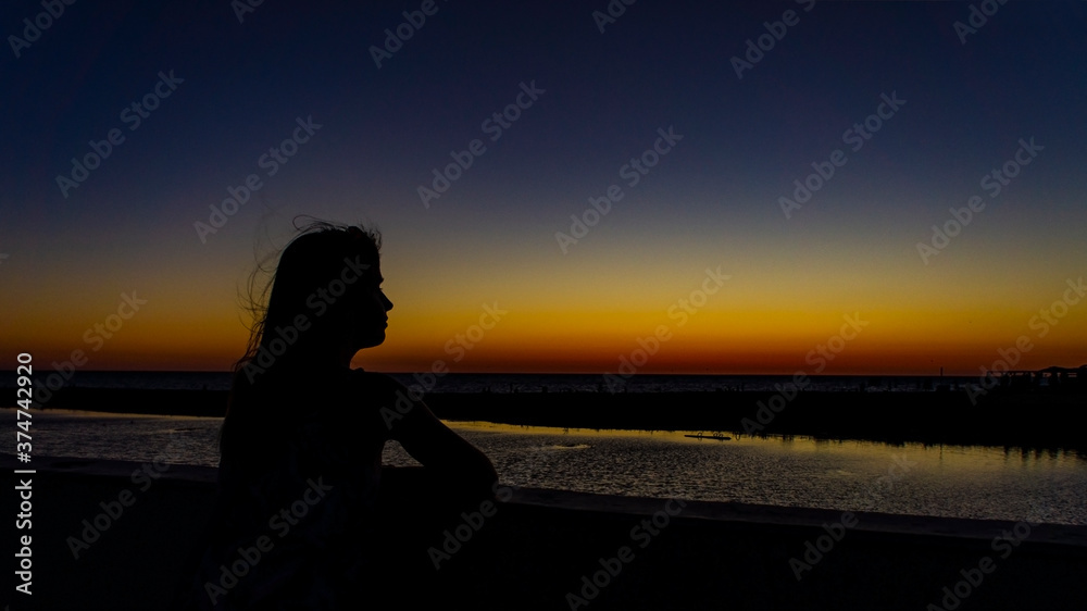 Fototapeta premium Silhouette of a young woman with fluttering hair against the background of a bright sunset
