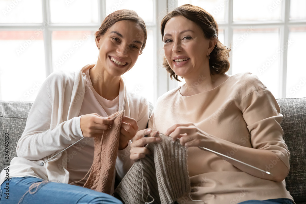 Φωτογραφία Portrait of smiling young woman resting on sofa with affectionate mature older mommy, holding knitting needles with threads in hands, involved in domestic hobby activity at peaceful weekend time