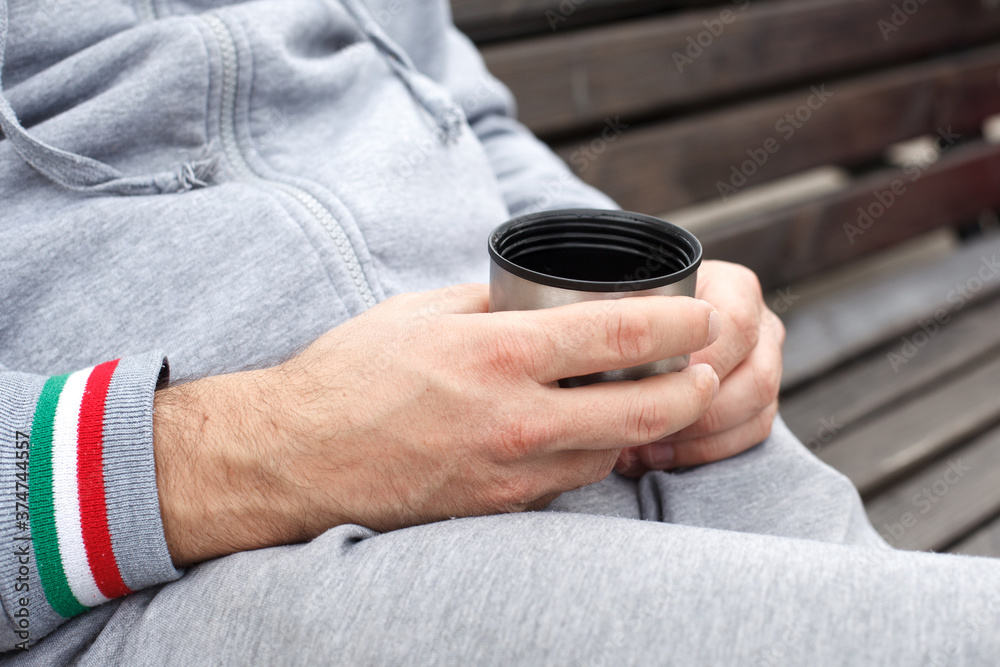 a man's hand holds a Cup of tea or coffee from a thermos