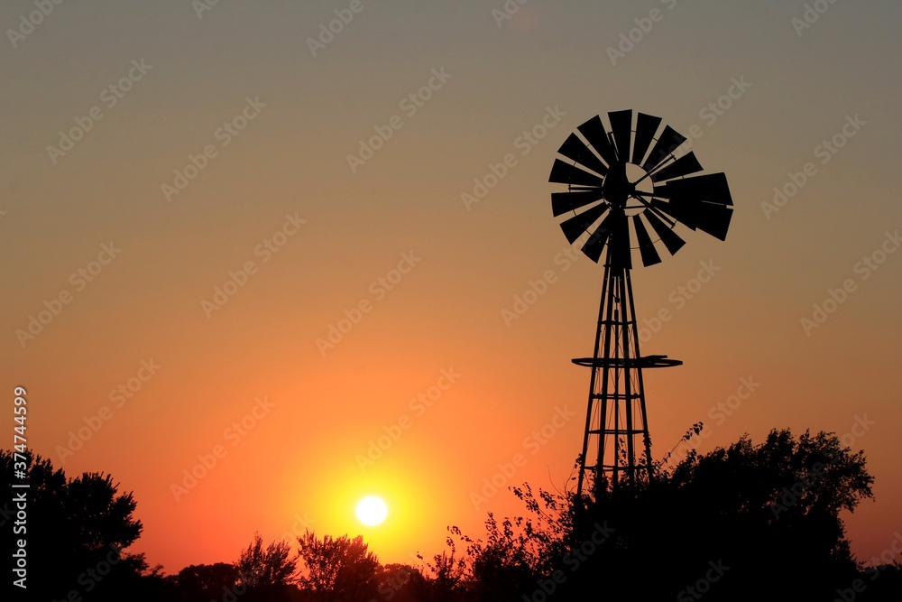 Kansas Sunset with a Windmill silhouette and tree's with a colorful sky.