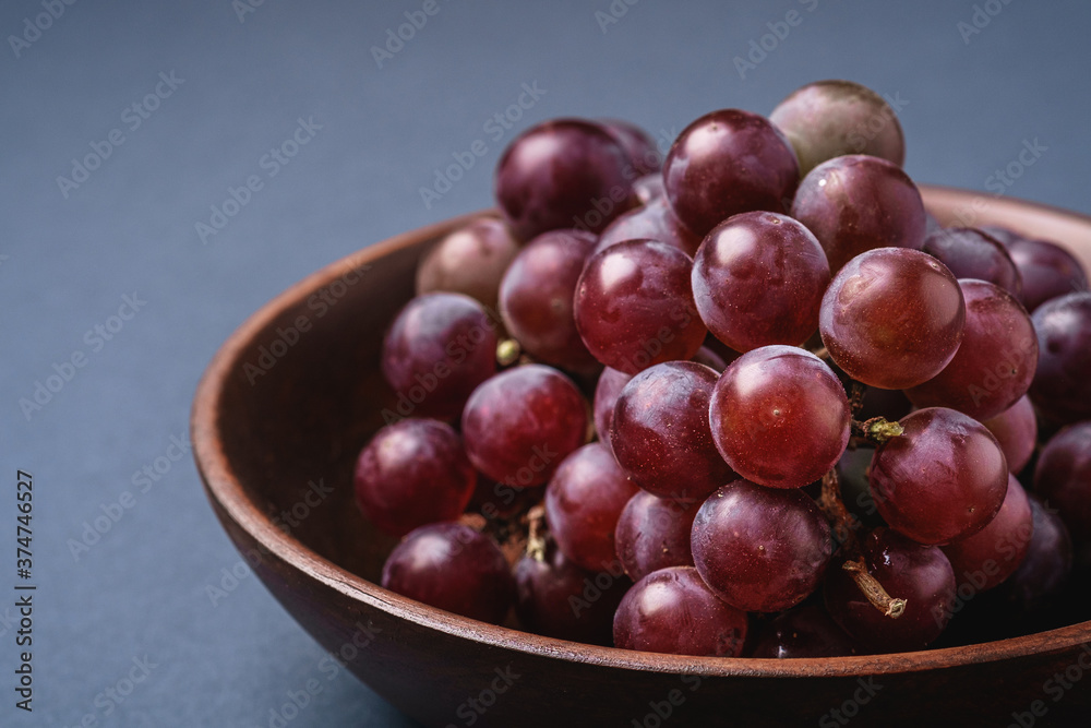 Fresh ripe grape berries in brown wooden bowl on blue grey minimal background, angle view macro Fresh ripe grape berries in brown wooden bowl on blue grey minimal background, angle view macro