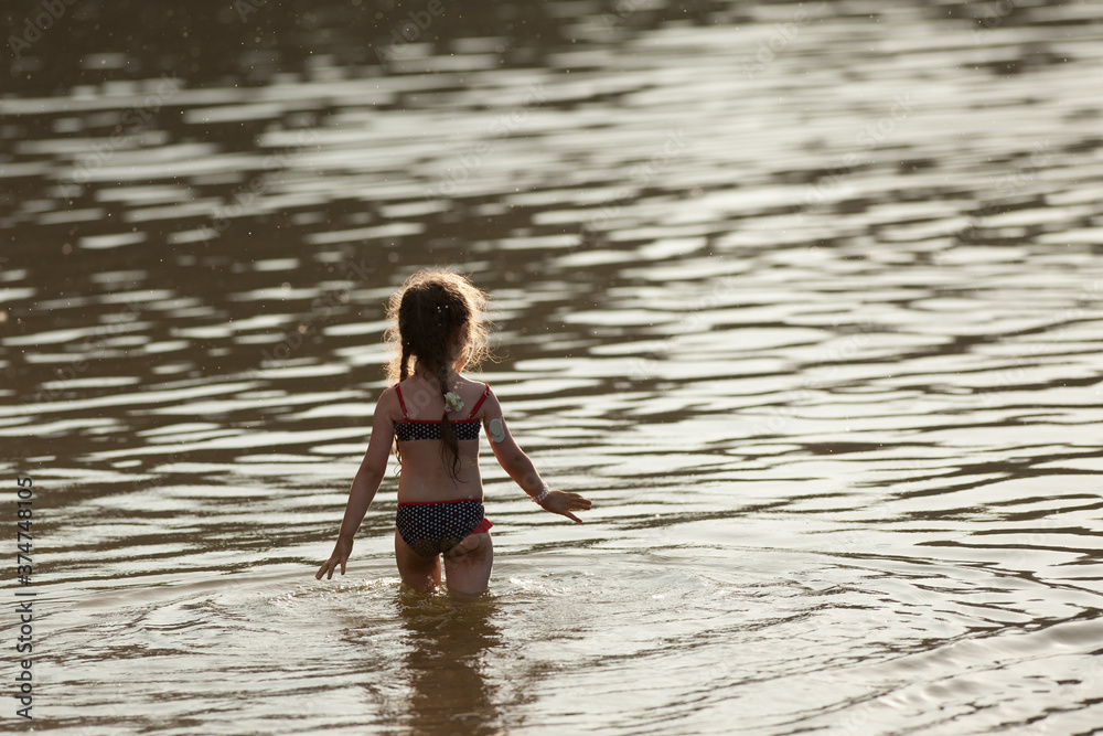 Fototapeta premium a girl with diabetes walks along the river bank in a swimsuit with a glucose diagnostic sensor on her arm.