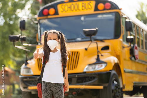 Concept of coronavirus COVID-19. Schoolgirl wearing medical face mask to health protection from influenza virus. Student girl with backpack and books - outdoors portrait. Child back to to school.