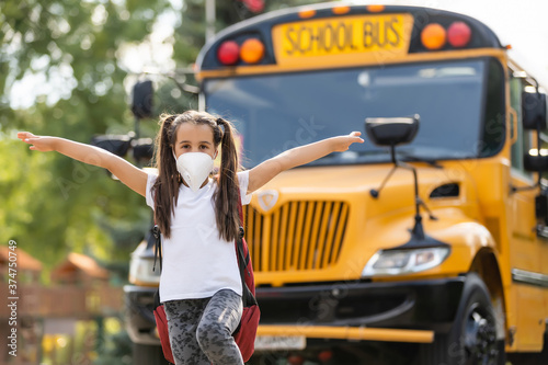 Concept of coronavirus COVID-19. Schoolgirl wearing medical face mask to health protection from influenza virus. Student girl with backpack and books - outdoors portrait. Child back to to school.