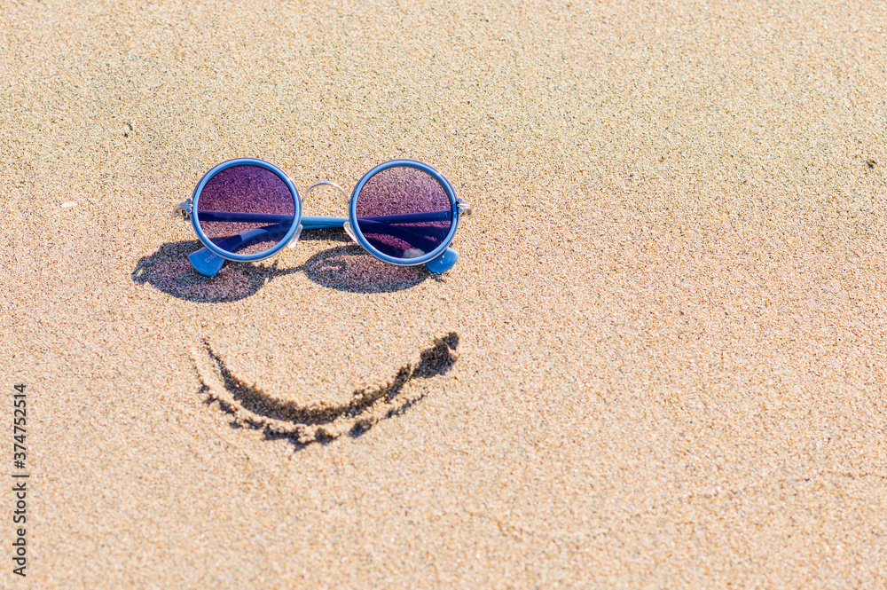 Sunglasses and a painted smile on a sandy beach. Travel concept