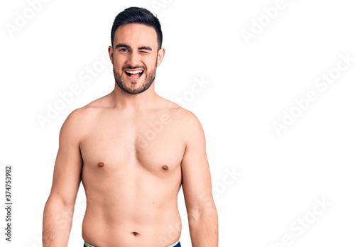 Young handsome man wearing swimwear winking looking at the camera with sexy expression  cheerful and happy face.