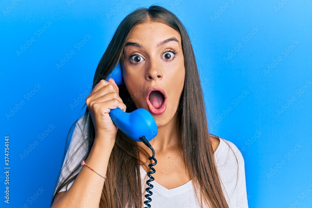 Young hispanic woman holding vintage telephone scared and amazed with open mouth for surprise, disbelief face - obrazy, fototapety, plakaty 