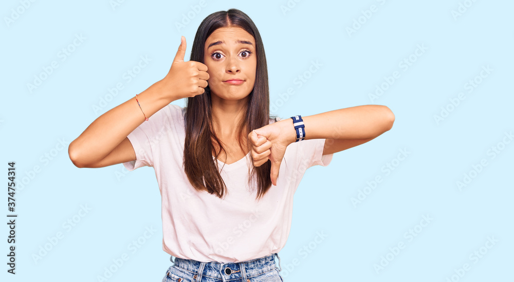 Young hispanic woman wearing casual white tshirt doing thumbs up and down, disagreement and agreement expression. crazy conflict Young hispanic woman wearing casual white tshirt doing thumbs up and down, disagreement and agreement expression. crazy conflict