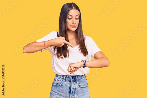 Young hispanic woman wearing casual white tshirt in hurry pointing to watch time, impatience, upset and angry for deadline delay
