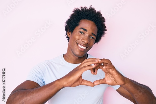 Handsome african american man with afro hair wearing casual clothes smiling in love showing heart symbol and shape with hands. romantic concept.