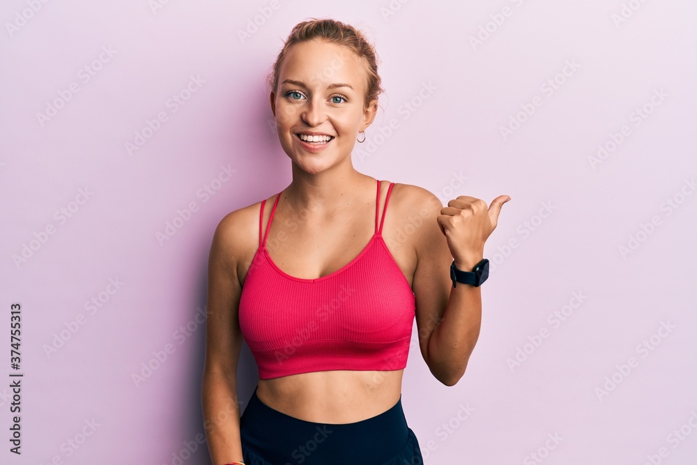 Beautiful caucasian woman wearing sportswear smiling with happy face looking and pointing to the side with thumb up. Beautiful caucasian woman wearing sportswear smiling with happy face looking and pointing to the side with thumb up.