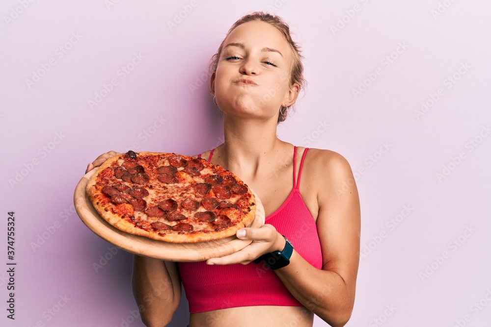Beautiful caucasian woman holding italian pizza puffing cheeks with funny face. mouth inflated with air, catching air. Beautiful caucasian woman holding italian pizza puffing cheeks with funny face. mouth inflated with air, catching air.