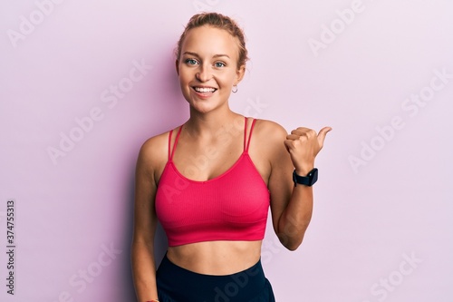 Beautiful caucasian woman wearing sportswear smiling with happy face looking and pointing to the side with thumb up. © Krakenimages.com