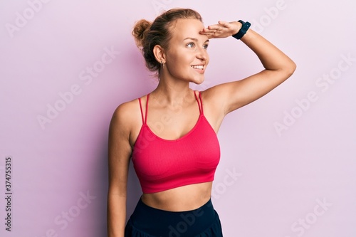 Beautiful caucasian woman wearing sportswear very happy and smiling looking far away with hand over head. searching concept. © Krakenimages.com