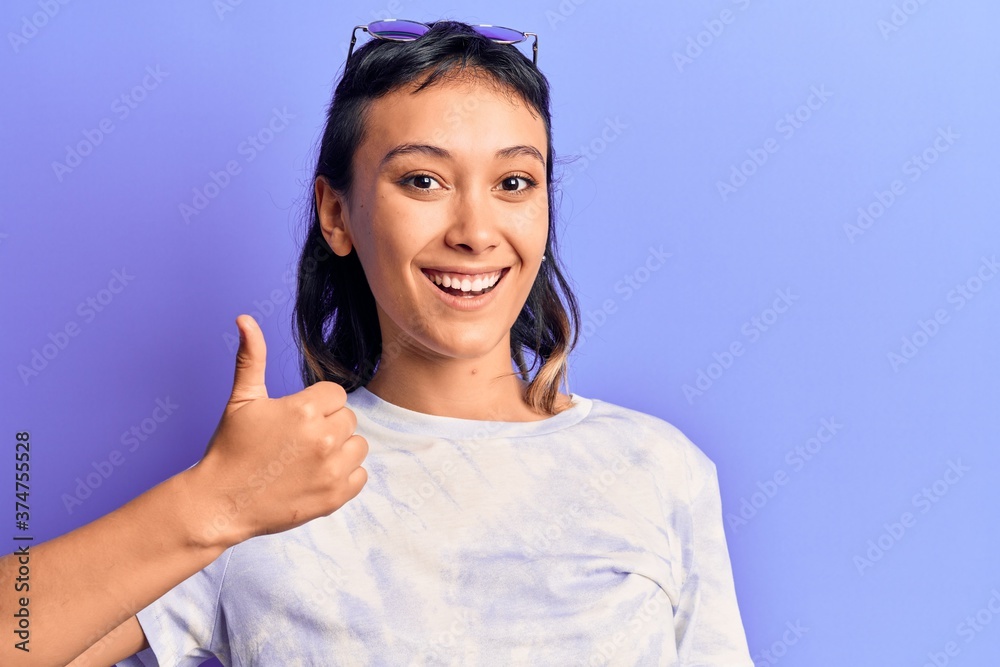 Young woman wearing casual clothes smiling happy and positive, thumb up doing excellent and approval sign Young woman wearing casual clothes smiling happy and positive, thumb up doing excellent and approval sign