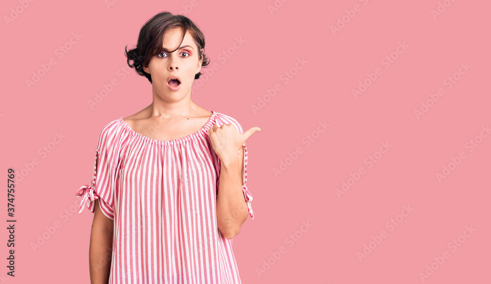 Beautiful young woman with short hair wearing casual summer clothes surprised pointing with hand finger to the side, open mouth amazed expression. Beautiful young woman with short hair wearing casual summer clothes surprised pointing with hand finger to the side, open mouth amazed expression.