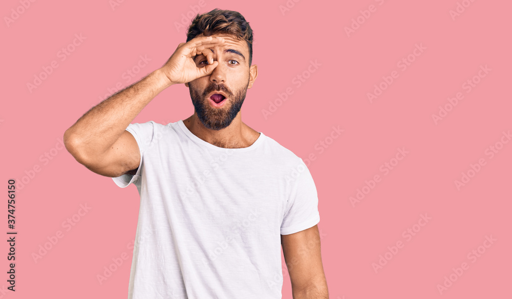 Fototapeta premium Young hispanic man wearing casual white tshirt doing ok gesture shocked with surprised face, eye looking through fingers. unbelieving expression.