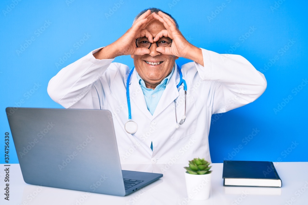 Senior handsome man with gray hair wearing doctor uniform working using computer laptop doing ok gesture like binoculars sticking tongue out, eyes looking through fingers. crazy expression. Senior handsome man with gray hair wearing doctor uniform working using computer laptop doing ok gesture like binoculars sticking tongue out, eyes looking through fingers. crazy expression.