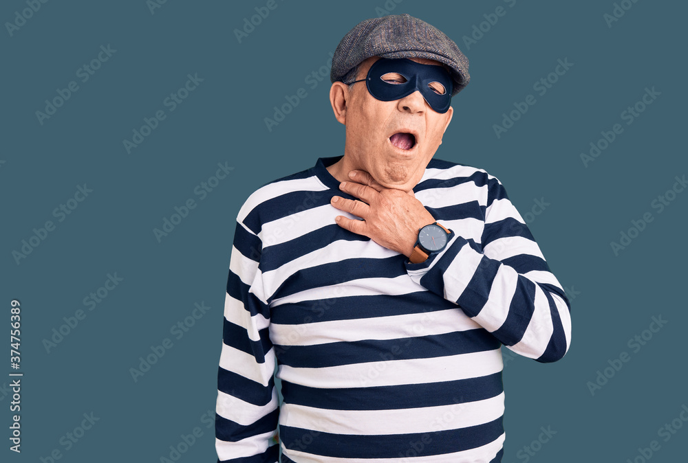 Senior handsome man wearing burglar mask and t-shirt touching painful neck, sore throat for flu, clod and infection