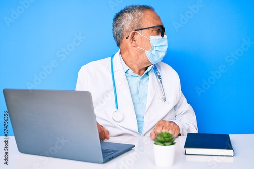 Senior handsome man with gray hair wearing doctor uniform and medical mask looking to side, relax profile pose with natural face with confident smile. © Krakenimages.com