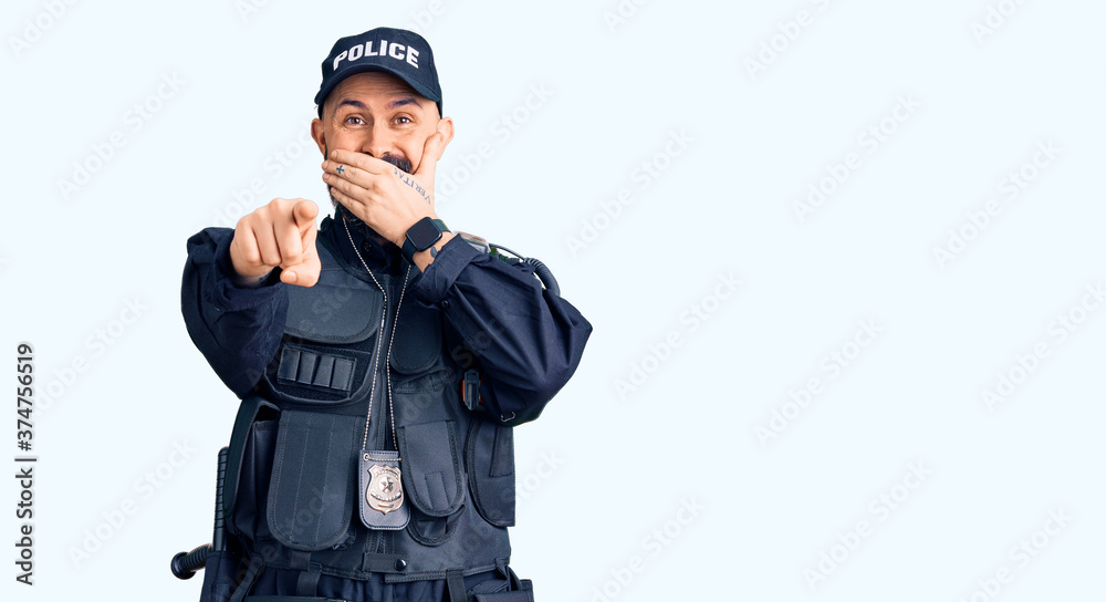 Young handsome man wearing police uniform laughing at you, pointing finger to the camera with hand over mouth, shame expression Young handsome man wearing police uniform laughing at you, pointing finger to the camera with hand over mouth, shame expression