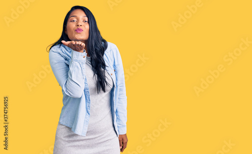 Hispanic woman with long hair wearing casual denim jacket looking at the camera blowing a kiss with hand on air being lovely and sexy. love expression. © Krakenimages.com